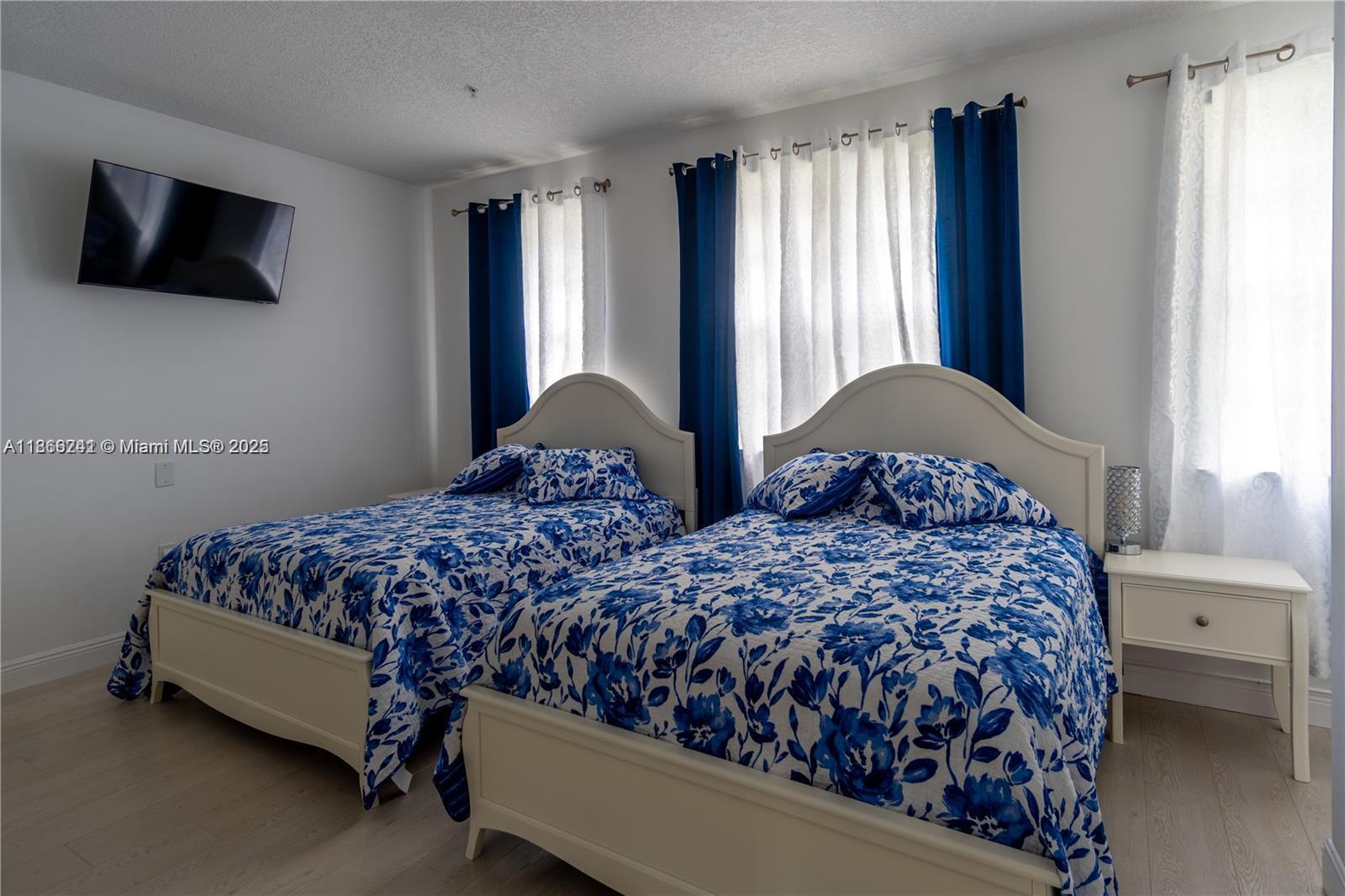 A bedroom features two beds with blue and white floral bedding and matching curtains — 2069 S Ocean Dr, Hallandale Beach FL 33009, HALLANDALE BEACH, FL