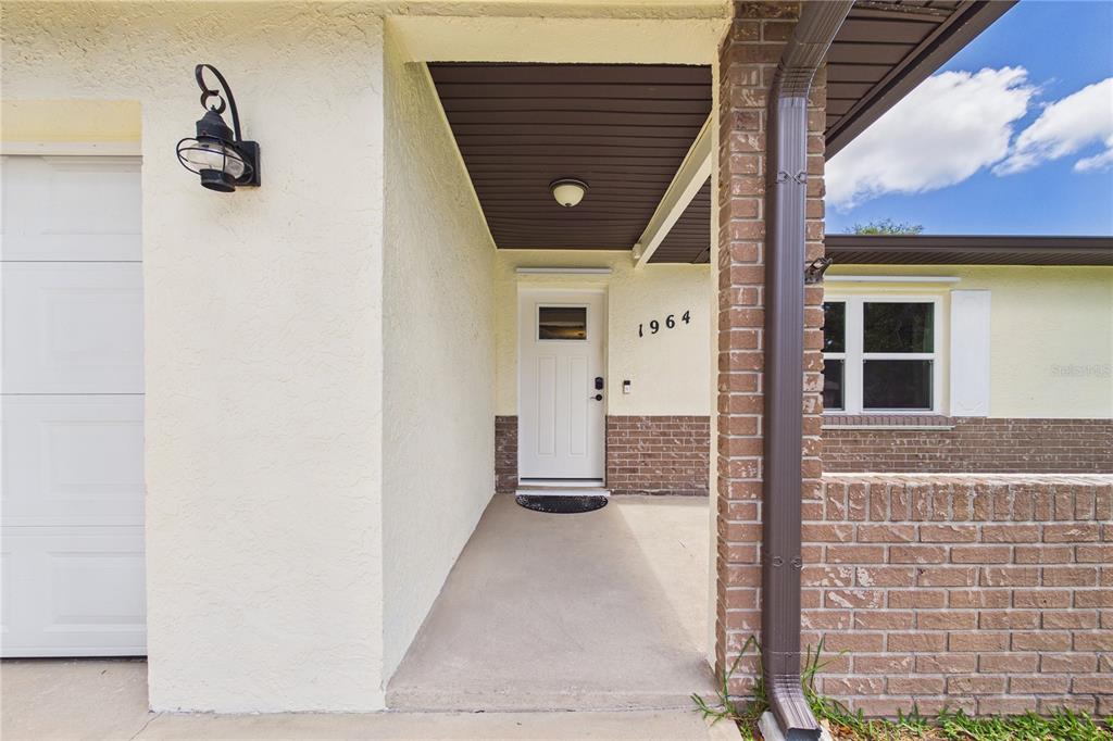 The exterior of a house features a white front door, brick accents, and a garage — 1964 W SHORES ROAD, MELBOURNE, FL