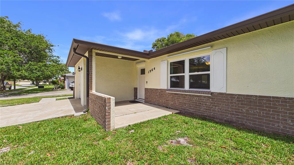 A single-story house exterior features a brick base, yellow stucco walls, and a covered porch — 1964 W SHORES ROAD, MELBOURNE, FL