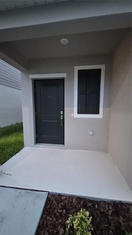 A covered concrete porch leads to a dark front door and a single shuttered window — 6220 BOTTICELLA BOULEVARD, WINTER HAVEN, FL