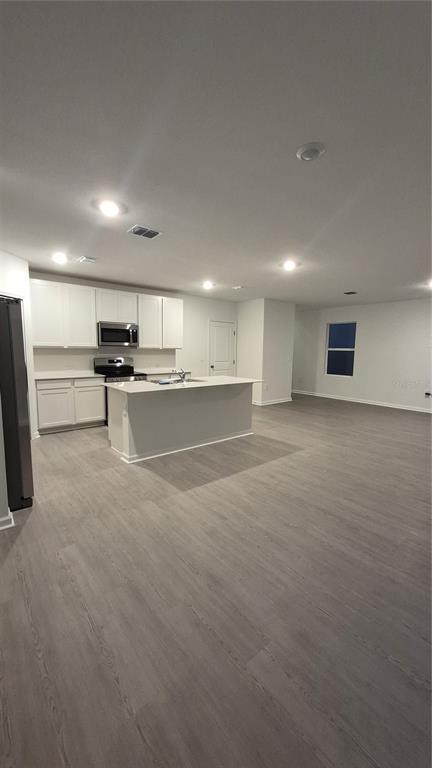 A modern kitchen features white cabinets, stainless steel appliances, a center island, and wood-look flooring — 6220 BOTTICELLA BOULEVARD, WINTER HAVEN, FL