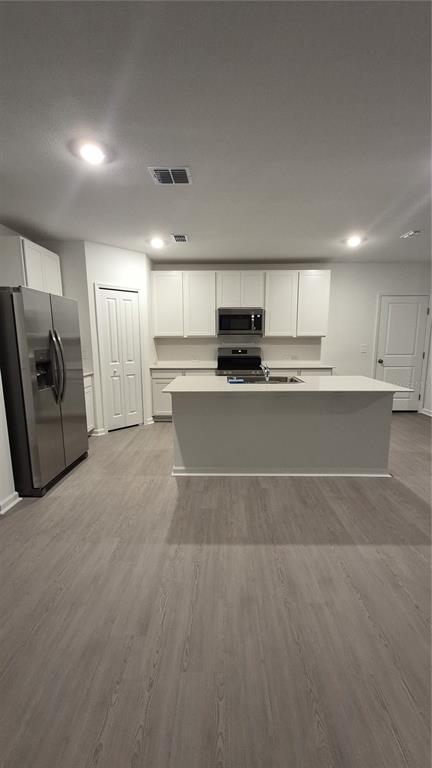 A kitchen with white cabinets, stainless steel appliances, a center island, and light wood flooring — 6220 BOTTICELLA BOULEVARD, WINTER HAVEN, FL