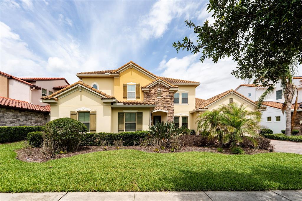 A two-story yellow stucco house with a tile roof and stone accents sits behind grass — 8530 BAYVIEW CROSSING DRIVE, WINTER GARDEN, FL