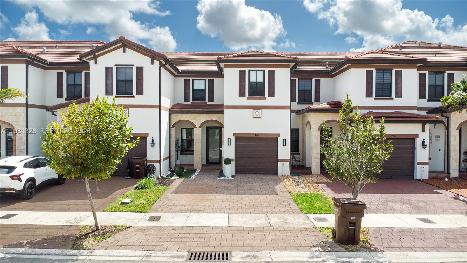 A row of two-story townhomes features white stucco facades, brown garage doors, and tiled roofs — 3438 W 104th Ter, Hialeah FL 33018, HIALEAH, FL
