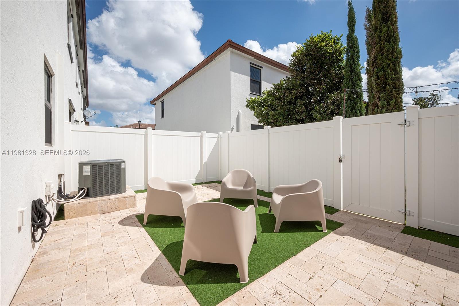 A small backyard patio features beige chairs on artificial turf surrounded by stone pavers — 3438 W 104th Ter, Hialeah FL 33018, HIALEAH, FL