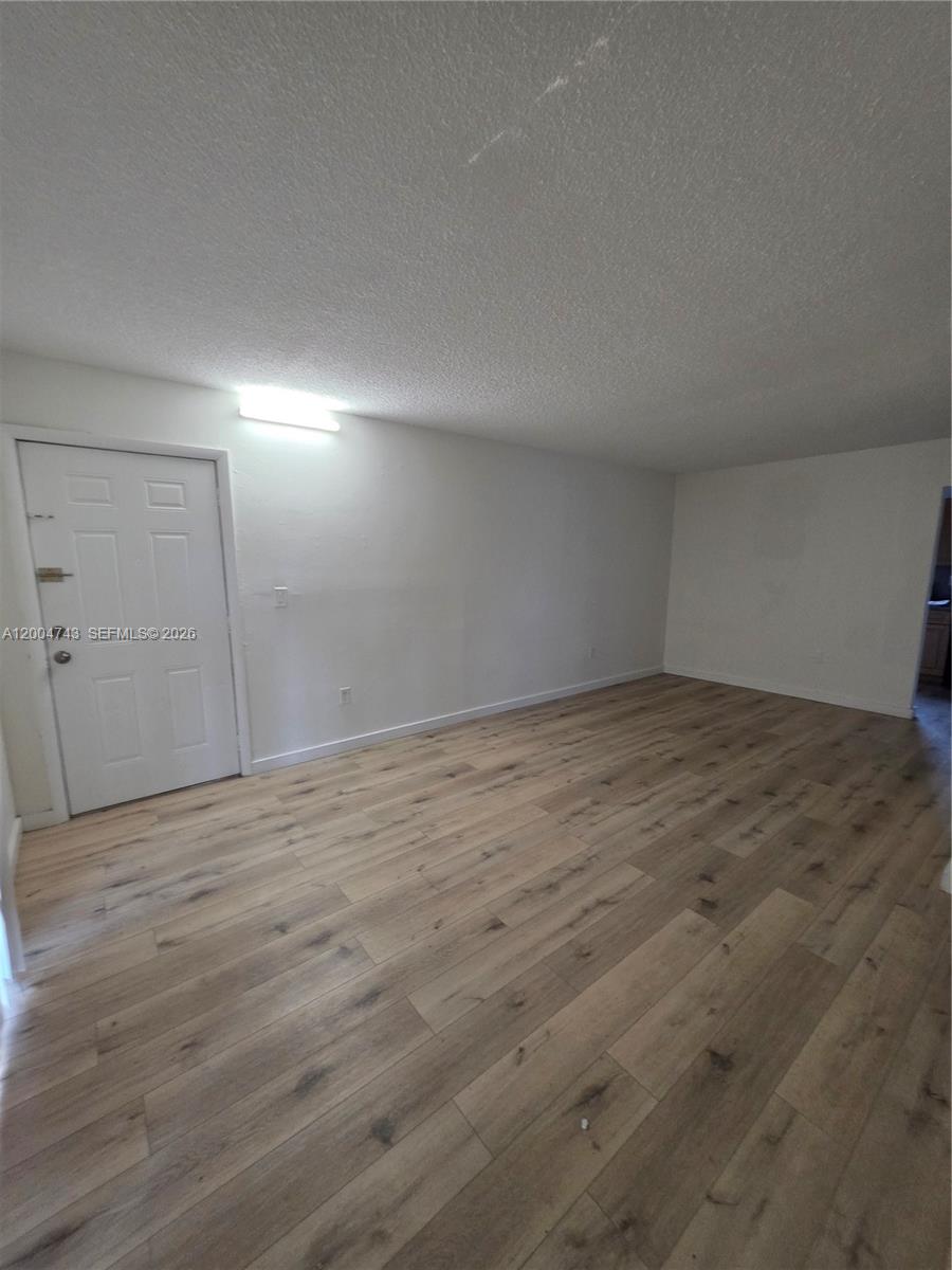 An empty room features light wood-look flooring, white walls, and a single white door — 1111 NW 19th Ave # 205, Miami FL 33125, MIAMI, FL