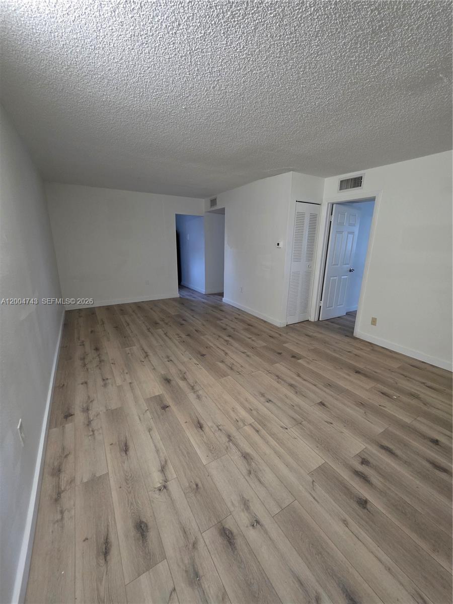 An empty room features light wood-look flooring, white walls, and a textured ceiling — 1111 NW 19th Ave # 205, Miami FL 33125, MIAMI, FL