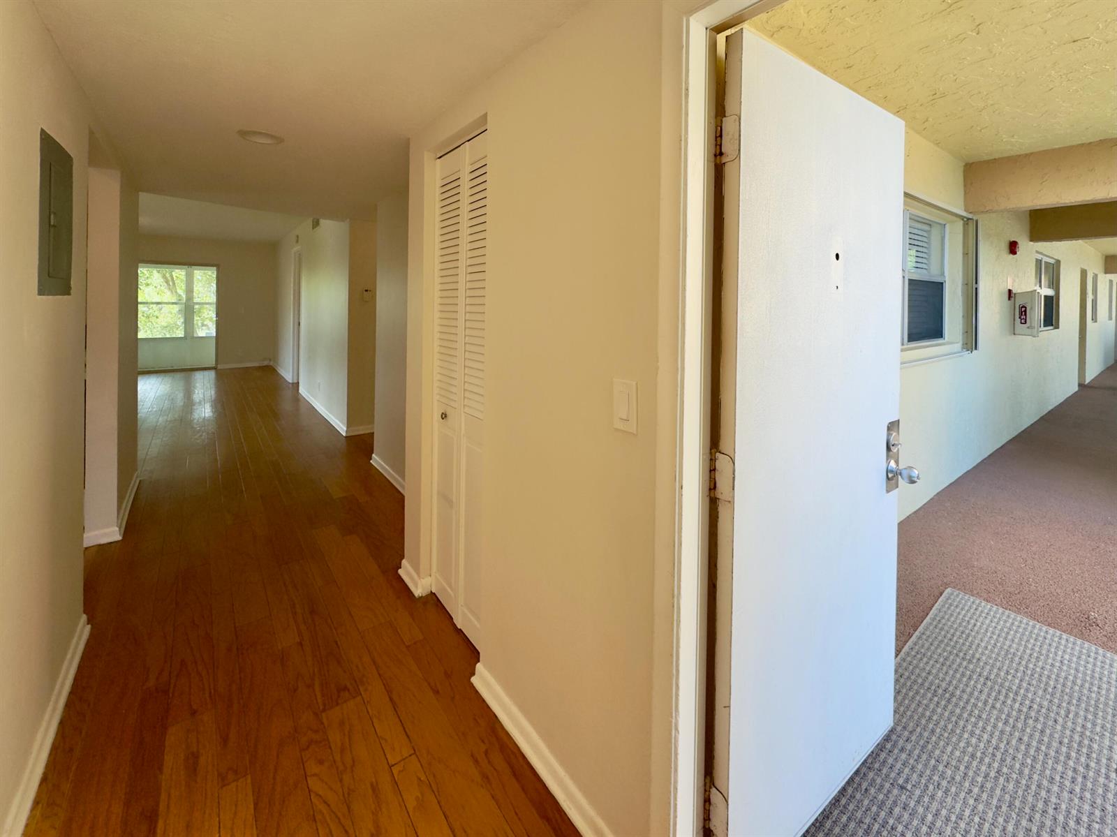 An open front door reveals a hallway with hardwood floors and a louvered closet door — 2800 Fiore Way # 201, Delray Beach FL 33445, DELRAY BEACH, FL