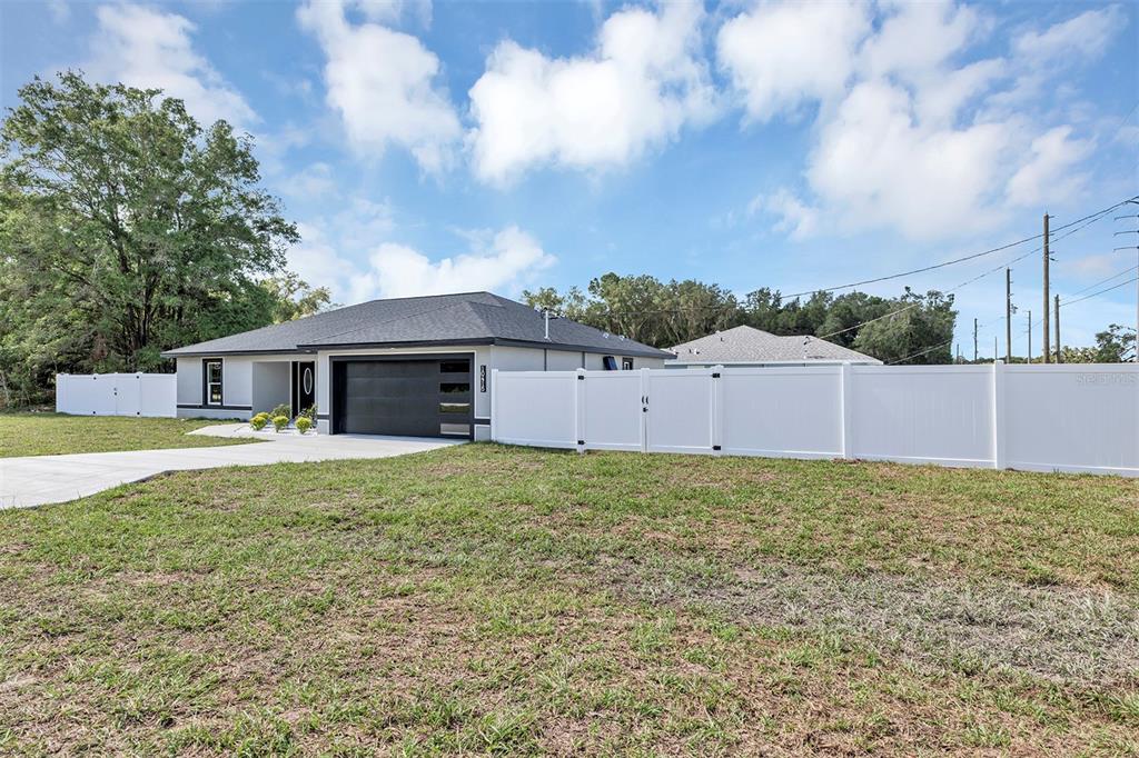 A modern single-story house with a black garage door and a white vinyl privacy fence — 10415 SW 140TH AVENUE, DUNNELLON, FL