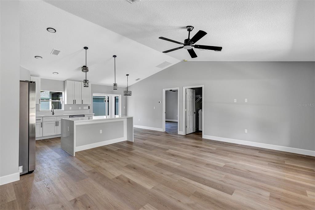 An open-concept kitchen and living area features light gray walls, wood-look flooring, and vaulted ceilings — 10415 SW 140TH AVENUE, DUNNELLON, FL