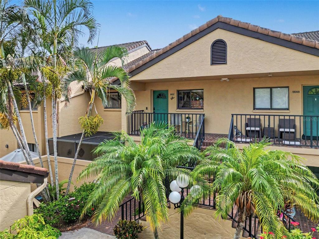An exterior view of a two-story building with balconies, palm trees, and a brick walkway — 5652 ASHTON LAKE DRIVE UNIT 5652, SARASOTA, FL