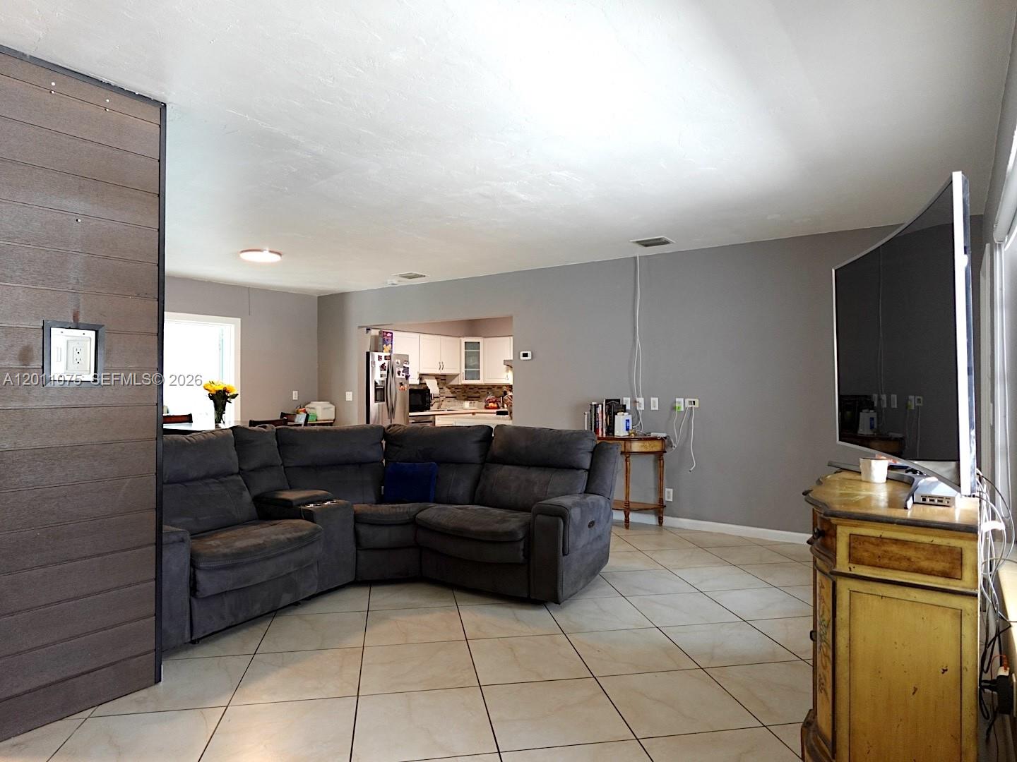 A living room features a large gray sectional sofa, tile flooring, and a wall-mounted television — 730 N 73rd Ave, Hollywood FL 33024, HOLLYWOOD, FL