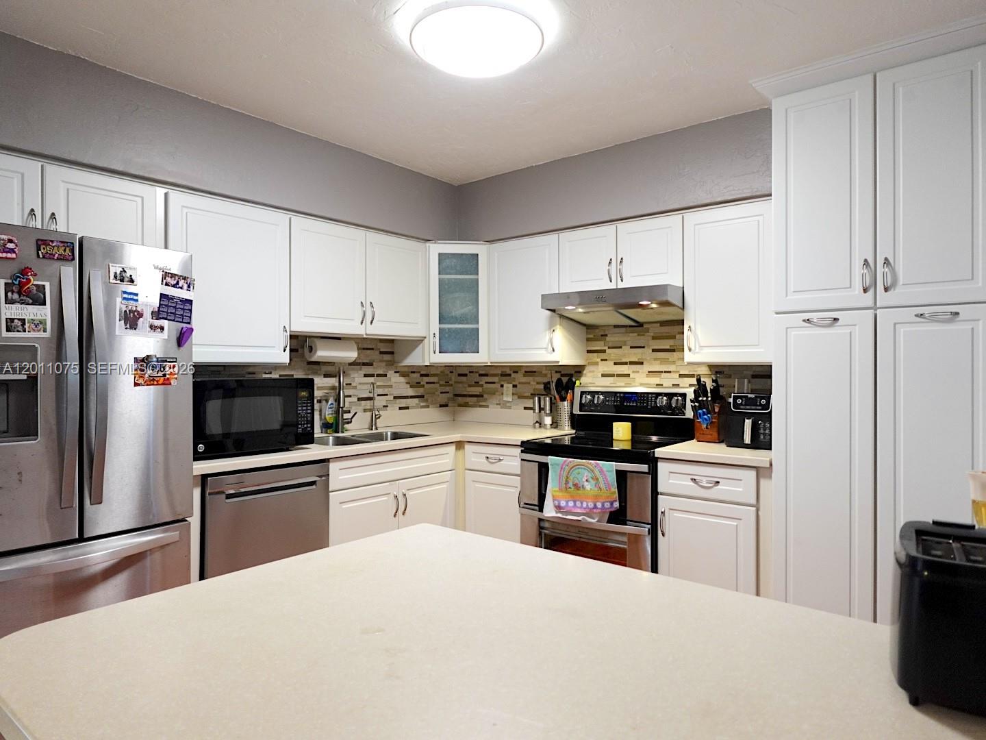 A kitchen features white cabinets, stainless steel appliances, a tiled backsplash, and a central island — 730 N 73rd Ave, Hollywood FL 33024, HOLLYWOOD, FL