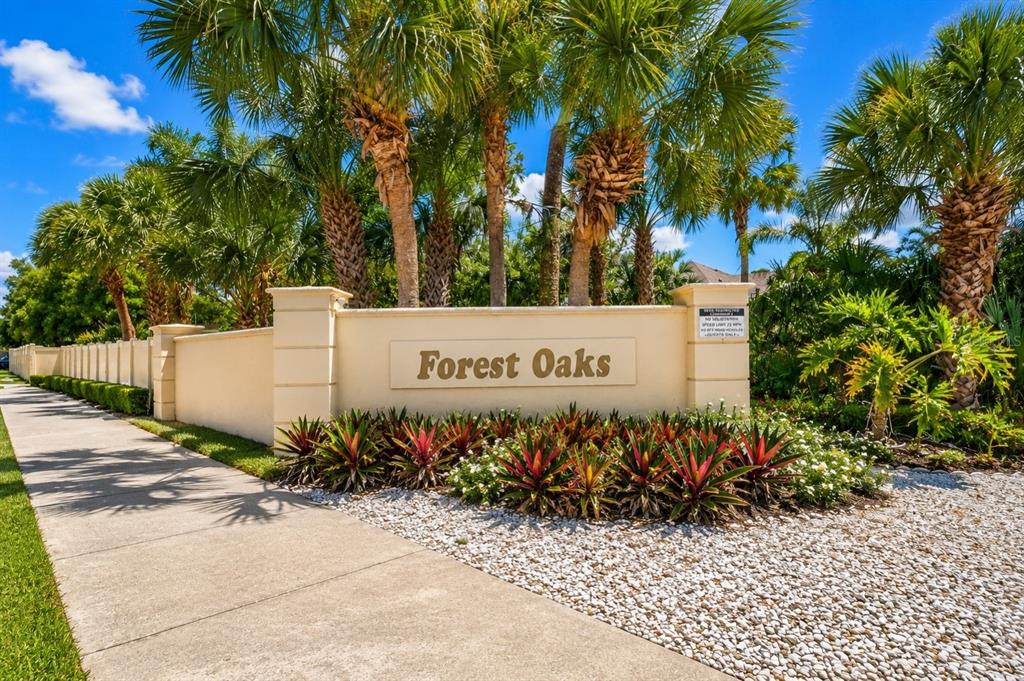 A beige stucco entrance sign for Forest Oaks stands behind a garden bed with palm trees — 5425 MATTHEW COURT, SARASOTA, FL