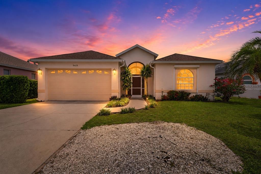 A single-story house with a two-car garage, arched entryway, and a concrete driveway at sunset — 5425 MATTHEW COURT, SARASOTA, FL