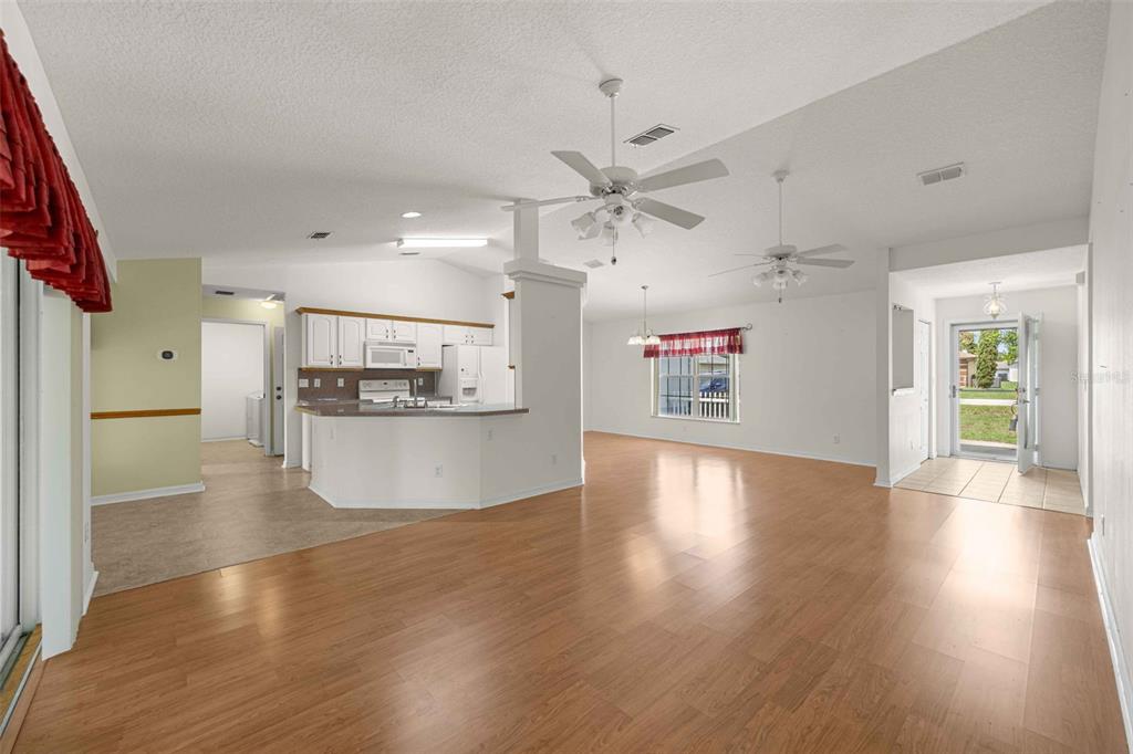 An open-concept living and kitchen area features light wood flooring, white cabinets, and ceiling fans — 8459 SW 60TH COURT, OCALA, FL