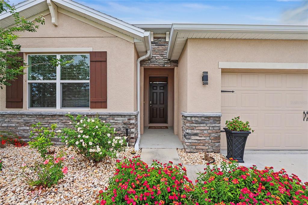 The exterior of a single-story house features a stone facade, a garage, and landscaped flowerbeds — 6265 SW 88 LOOP, OCALA, FL