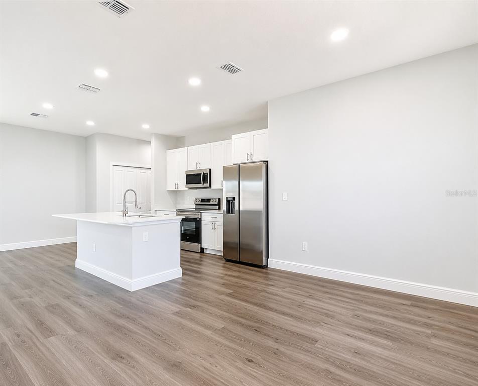 A modern kitchen features white cabinetry, stainless steel appliances, a center island, and wood-look flooring — 39 WATER TRACK DRIVE, OCALA, FL