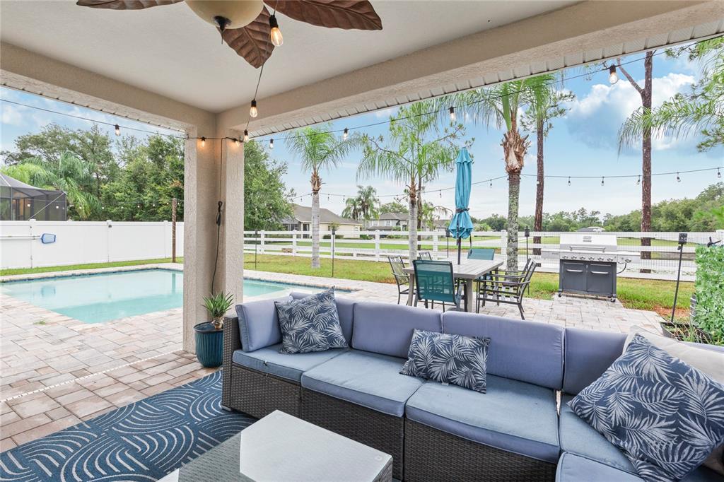 A covered patio features a sectional sofa, dining set, and pool overlooking a fenced yard — 20744 ORCHARDTOWN DRIVE, LAND O LAKES, FL