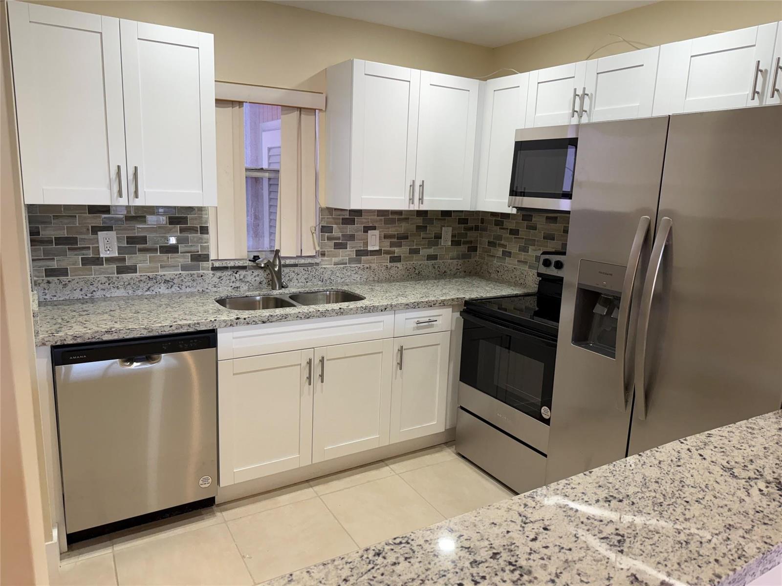 A kitchen features white cabinets, granite countertops, stainless steel appliances, and a tiled backsplash — 1450 N Riverside Drive # 204, Pompano Beach FL 33062, POMPANO BEACH, FL