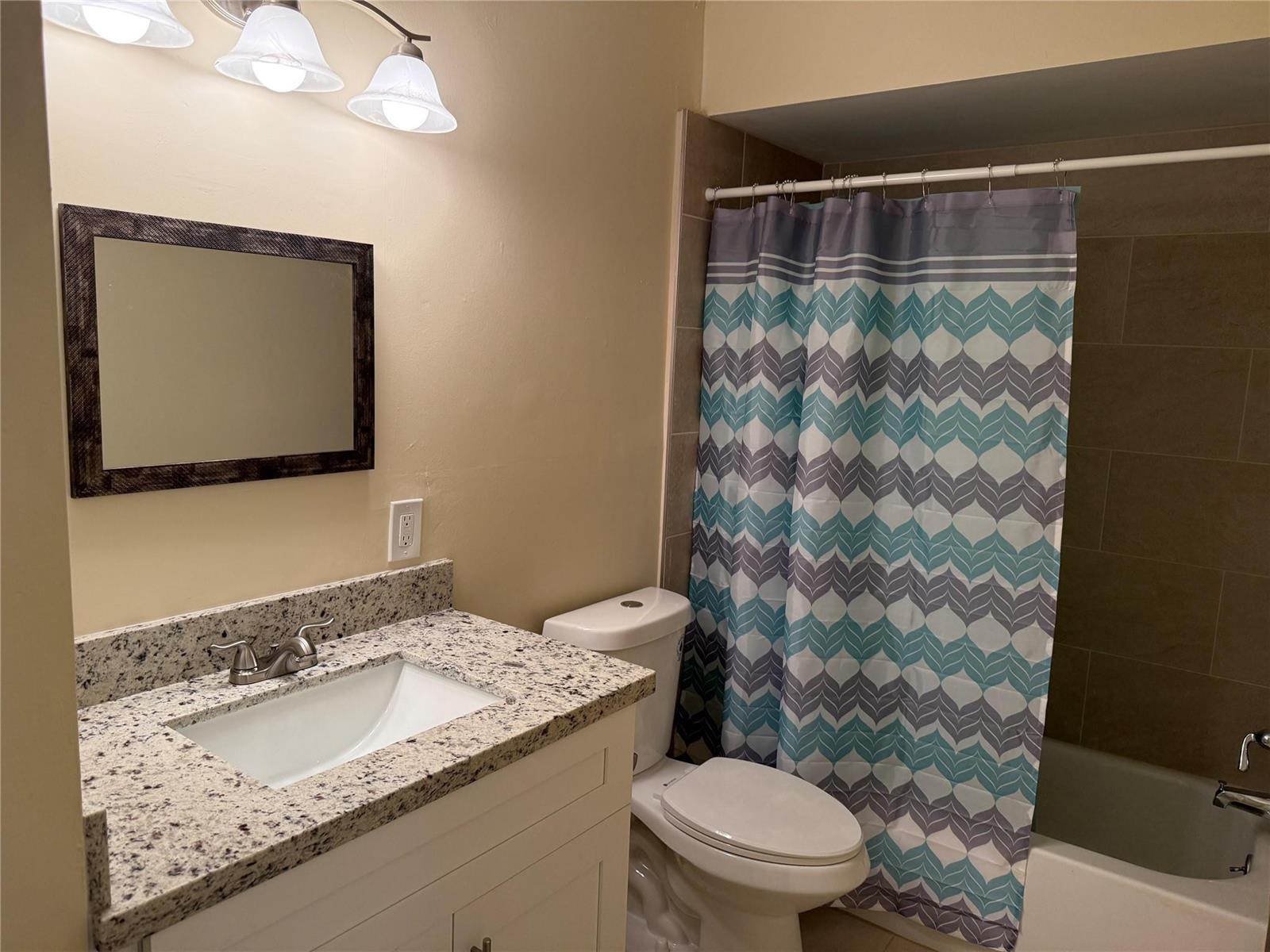 A bathroom features a granite vanity, a white cabinet, a toilet, and a patterned shower curtain — 1450 N Riverside Drive # 204, Pompano Beach FL 33062, POMPANO BEACH, FL