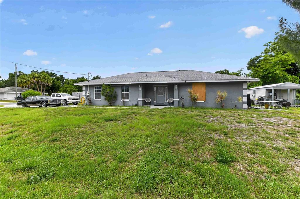 A single-story gray house with a boarded-up window and a detached carport on the right — 1904 2ND AVENUE E, PALMETTO, FL