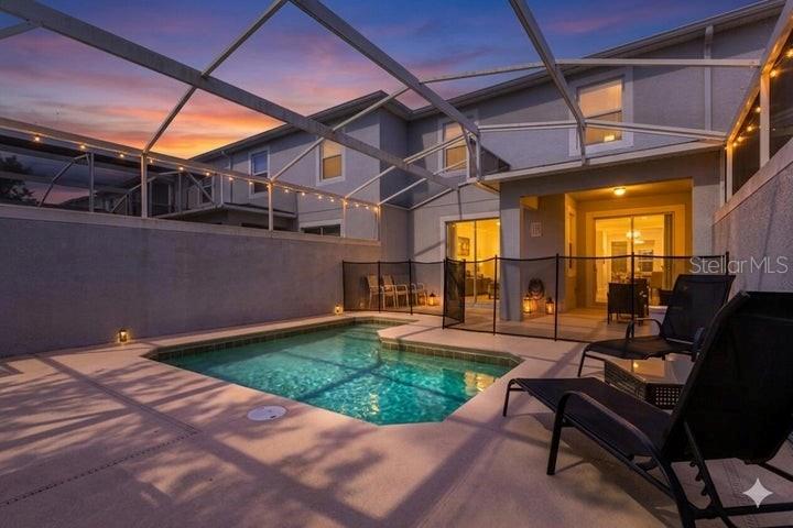 A screened-in swimming pool sits on a concrete patio next to a two-story house — 650 PEBBLE BEACH DRIVE, DAVENPORT, FL