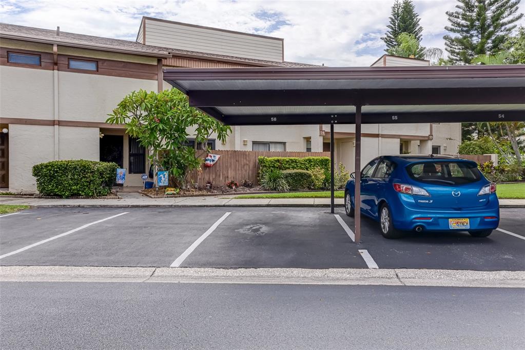 A blue hatchback is parked under a covered carport in front of a residential building — 9209 SEMINOLE BOULEVARD UNIT 56, SEMINOLE, FL