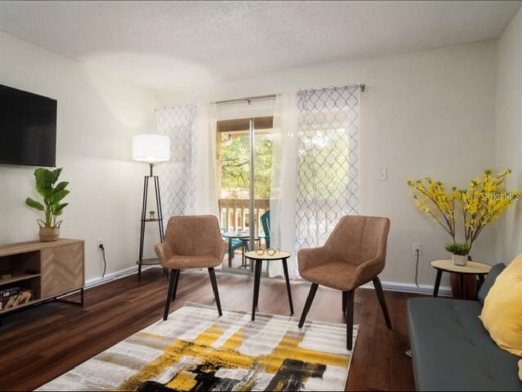 A living room features wood-look flooring, two brown chairs, a patterned rug, and sliding doors — 1810 NW 23RD BOULEVARD UNIT 178, GAINESVILLE, FL