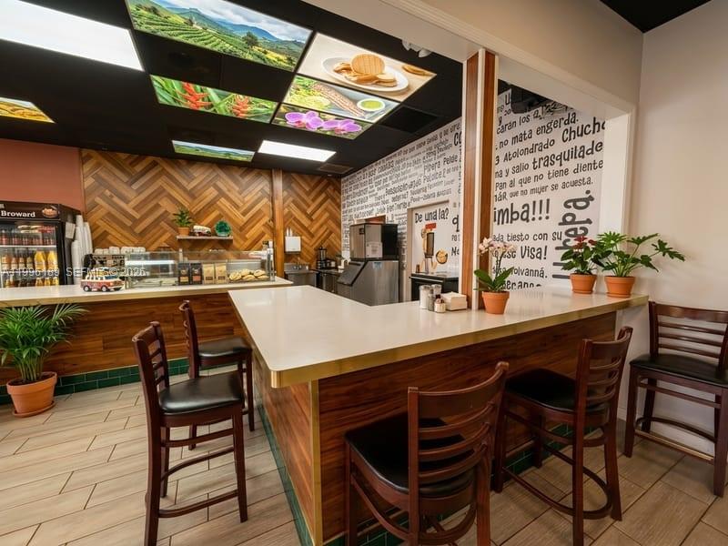 A restaurant interior features a white L-shaped counter, wooden bar stools, and a herringbone-patterned wall — N State Road 7, Tamarac FL 33319, TAMARAC, FL