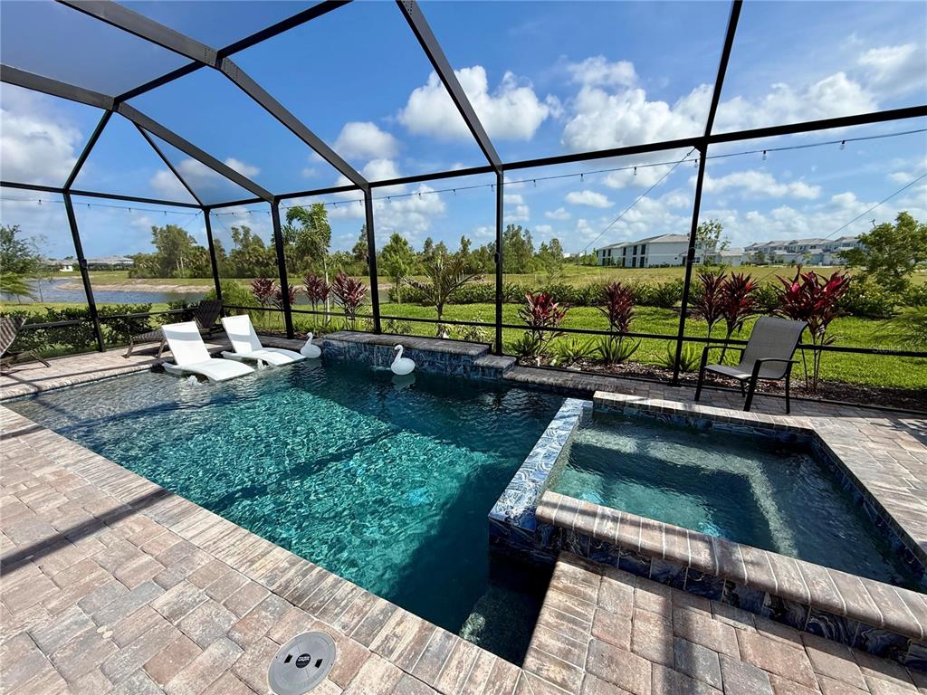 A screened-in pool and spa area with paver decking overlooking a pond and landscape — 10852 SUN DROP STREET, VENICE, FL