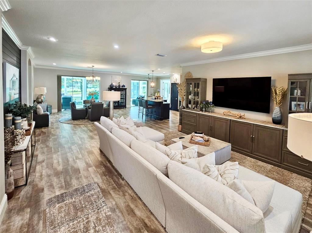 A spacious open-concept living room features a large sectional sofa, wood-look flooring, and media cabinetry — 1040 COTTAGE DRIVE, THE VILLAGES, FL