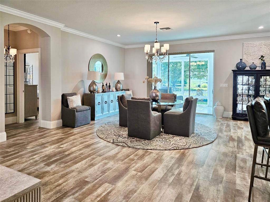 A dining room features a round table, gray upholstered chairs, a sideboard, and wood-look flooring — 1040 COTTAGE DRIVE, THE VILLAGES, FL