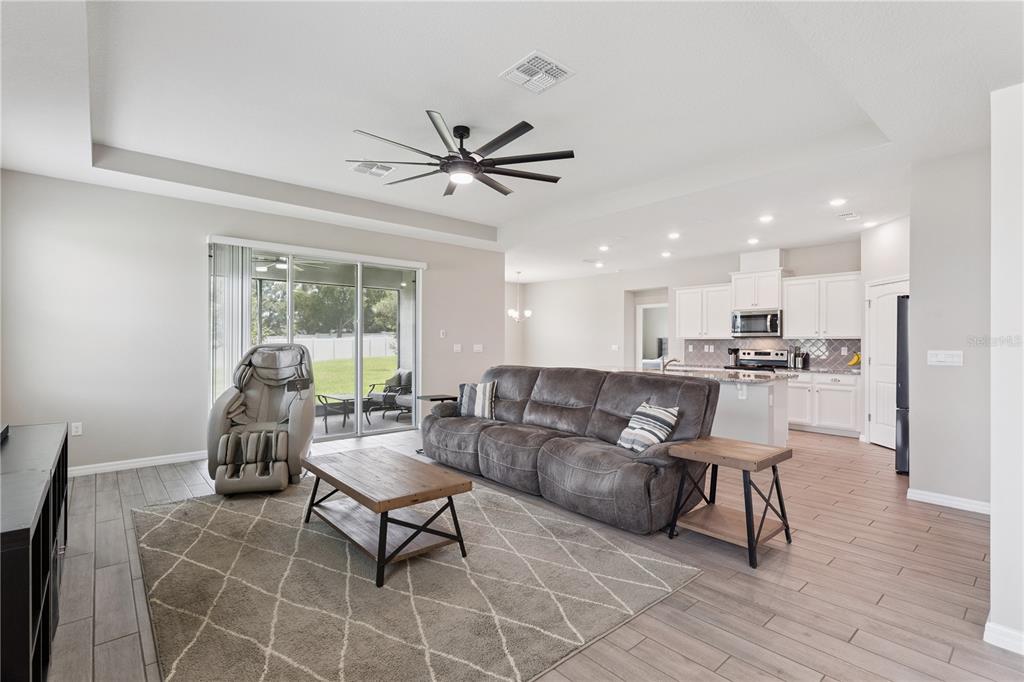 An open-concept living room with a grey sofa, coffee table, and kitchen in the background — 17954 HITHER HILLS CIRCLE, WINTER GARDEN, FL