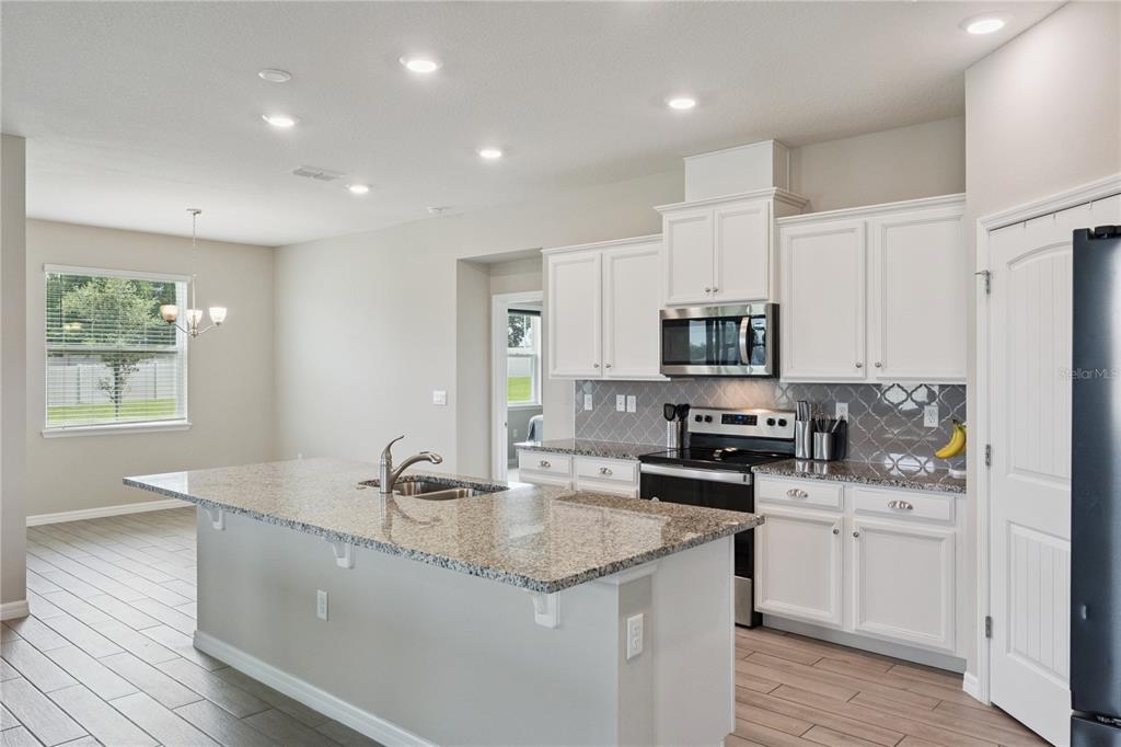 A kitchen with white cabinets, granite countertops, a center island, and wood-look tile flooring — 17954 HITHER HILLS CIRCLE, WINTER GARDEN, FL