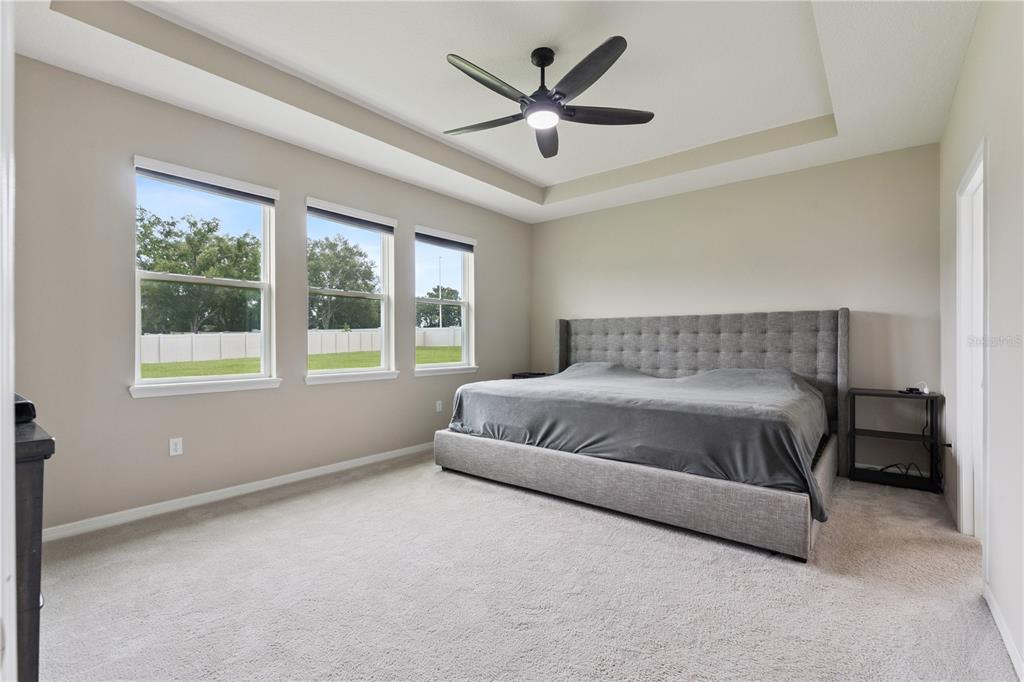 A bedroom features a tufted gray bed, a tray ceiling with a fan, and three windows — 17954 HITHER HILLS CIRCLE, WINTER GARDEN, FL