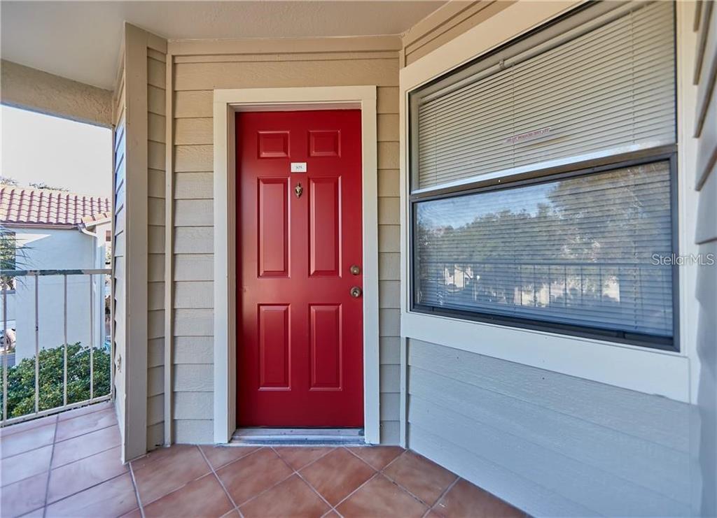 A red front door with a small window sits on a tiled balcony — 3032 PARKWAY BOULEVARD UNIT 305, KISSIMMEE, FL