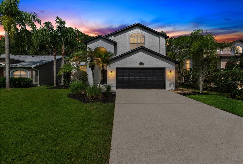 A two-story house with a white stucco exterior, a black garage door, and a concrete driveway — 13115 ROYAL GEORGE AVENUE, ODESSA, FL