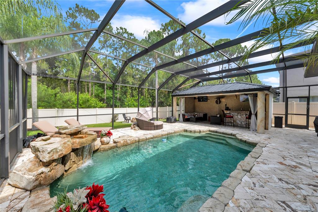 A screened-in pool area features a rock waterfall, stone decking, and a covered outdoor bar — 13115 ROYAL GEORGE AVENUE, ODESSA, FL