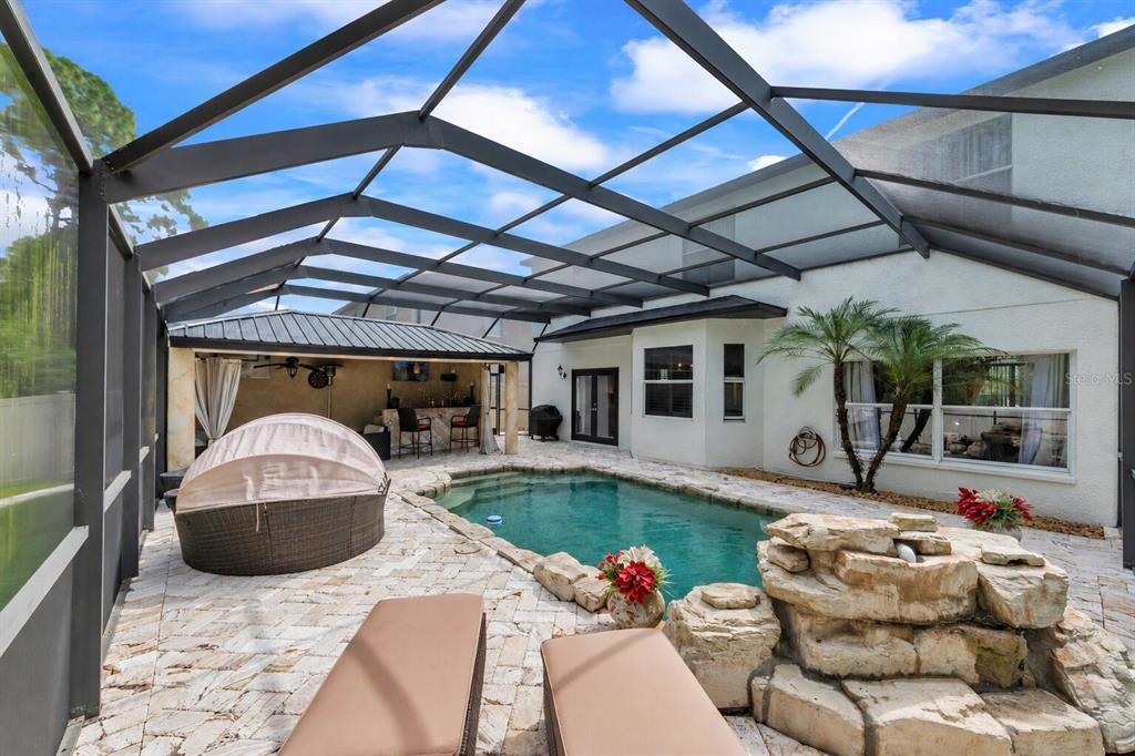 A screened-in patio features a swimming pool, a rock waterfall, and a covered outdoor bar — 13115 ROYAL GEORGE AVENUE, ODESSA, FL