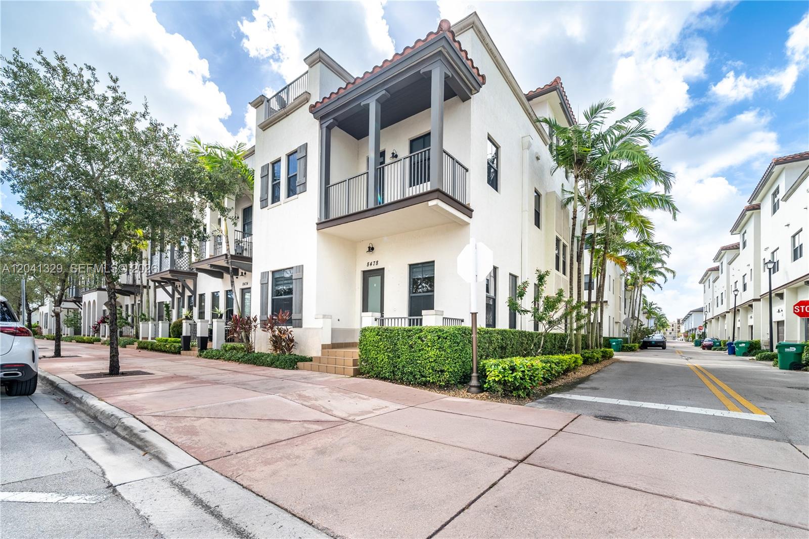 A three-story townhouse with a balcony, stucco exterior, and a manicured hedge in front — 8478 NW 52nd St, Doral FL 33166, DORAL, FL