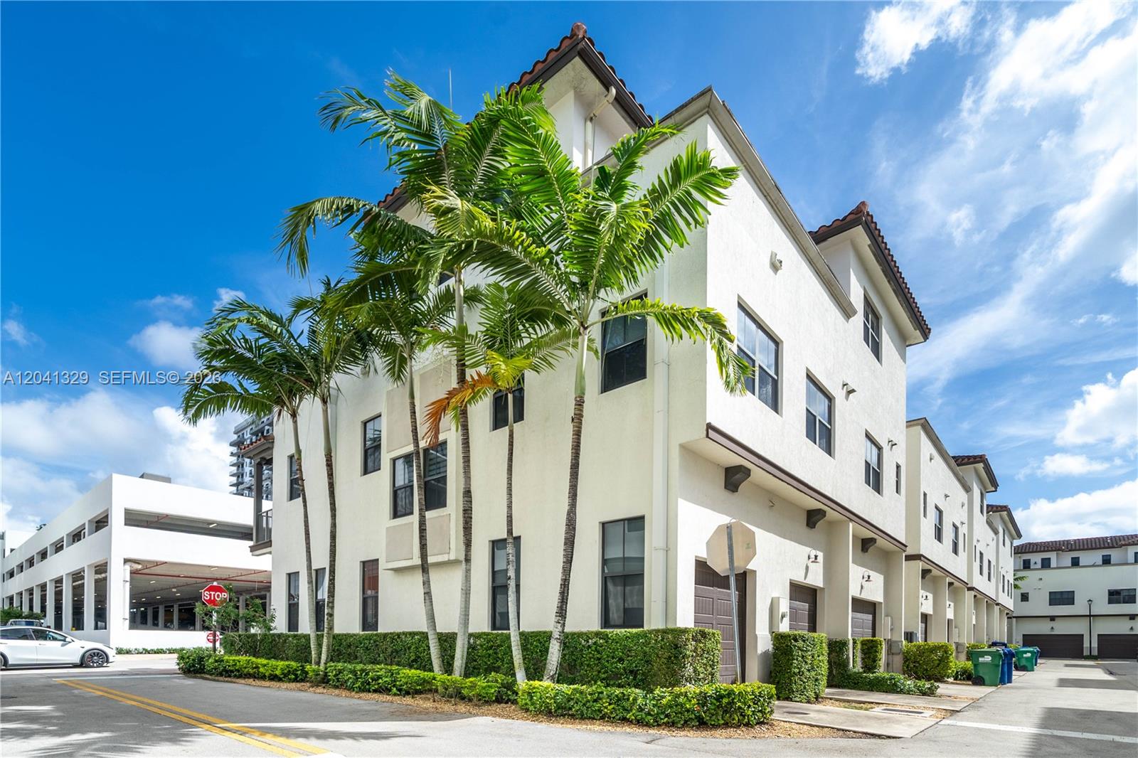 A multi-story townhouse exterior features white stucco walls, palm trees, and a row of garages — 8478 NW 52nd St, Doral FL 33166, DORAL, FL