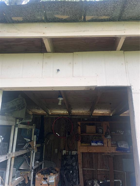 A view into a cluttered storage shed with exposed wooden rafters and a single lightbulb — 1218 CR 416N, LAKE PANASOFFKEE, FL