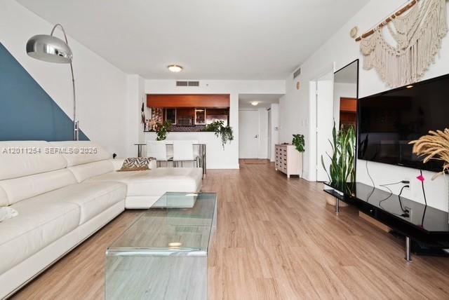 A living room features a white sectional sofa, a glass coffee table, and wood flooring — 1800 N Bayshore Dr # 1604, Miami FL 33132, MIAMI, FL