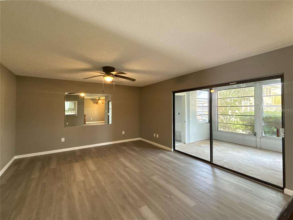 A living room with wood-look flooring, a ceiling fan, a wall mirror, and sliding glass doors — 22333 EDGEWATER DRIVE UNIT B1, PORT CHARLOTTE, FL