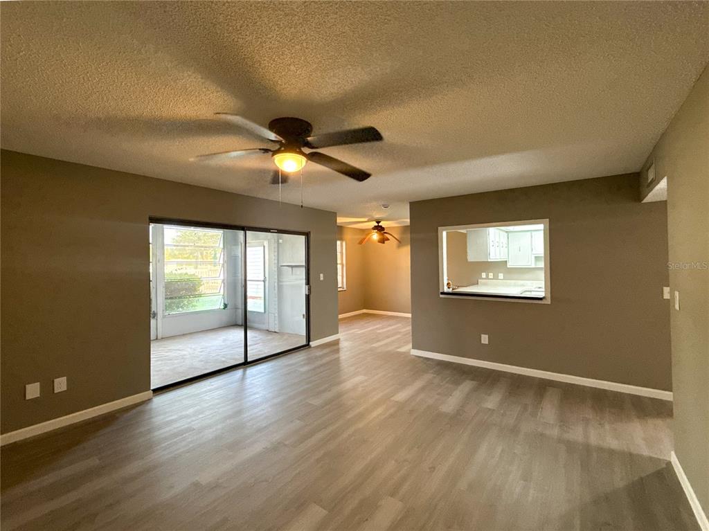 An interior view of a living room with wood-look flooring, a ceiling fan, and a pass-through window — 22333 EDGEWATER DRIVE UNIT B1, PORT CHARLOTTE, FL