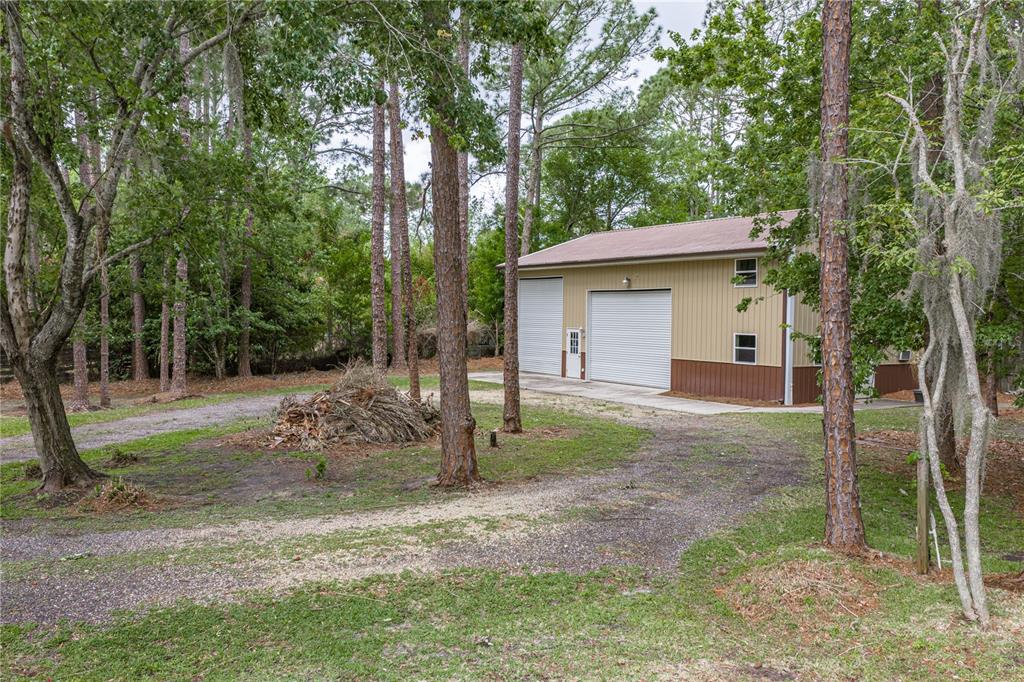 A detached metal garage sits on a gravel driveway surrounded by trees and brush — 7601 THUNDERHEAD STREET, WESLEY CHAPEL, FL