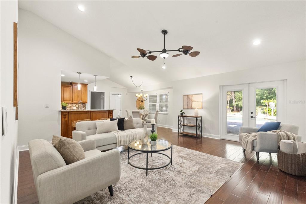 A living room with hardwood floors, a neutral sofa, and a view of a pool — 7601 THUNDERHEAD STREET, WESLEY CHAPEL, FL