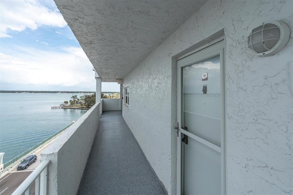 A balcony with a gray floor overlooks a body of water next to a door — 285 107TH AVENUE UNIT 701, TREASURE ISLAND, FL