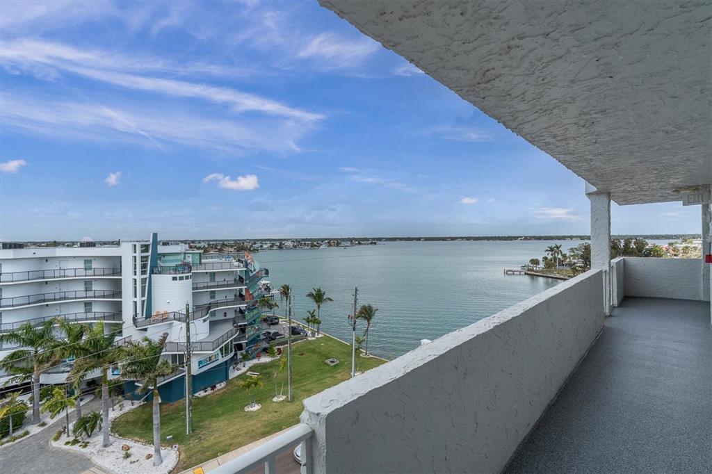 A view from a high-rise balcony overlooking a bay, palm trees, and a neighboring building — 285 107TH AVENUE UNIT 701, TREASURE ISLAND, FL